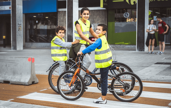 Drie kinderen in fluo-hesjes staan met de fiets op een zebrapad