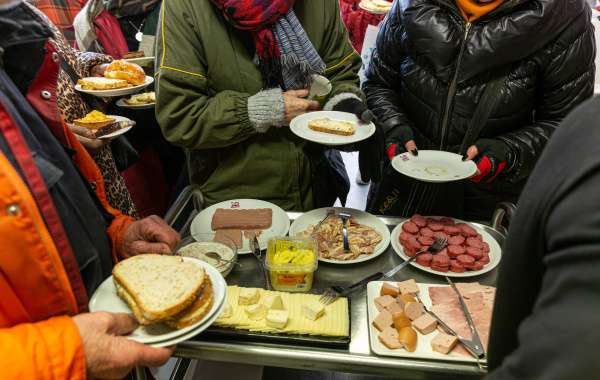 Photo avec des bénéficiaires tenant des assiettes remplies ou non, au-dessus d'un chariot avec de la nourriture pour le petit-déjeuner. Par respect de la vie privée, l'image ne montre pas de visages.